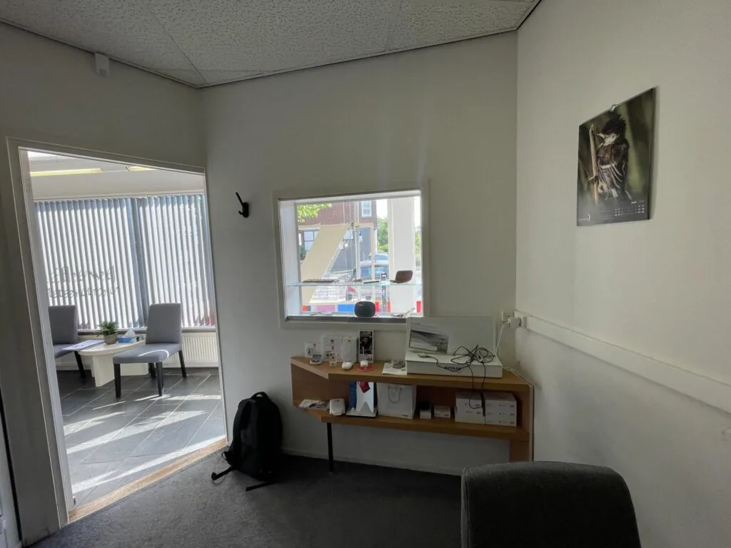 Kantoorruimte aan de Prinses Mariannelaan met een zithoek, wandplank met apparaten en een raam met uitzicht op de straat.